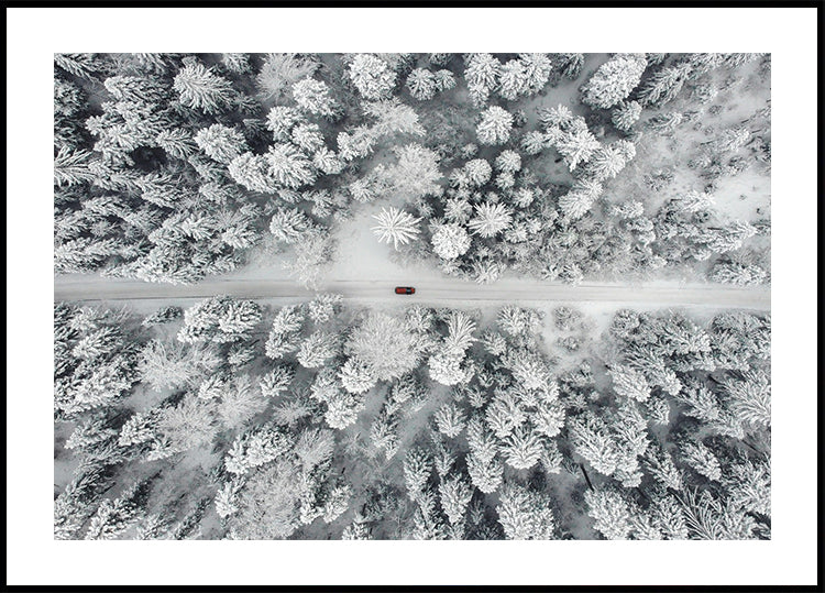 Punainen auto ajamassa lumisen metsän läpi