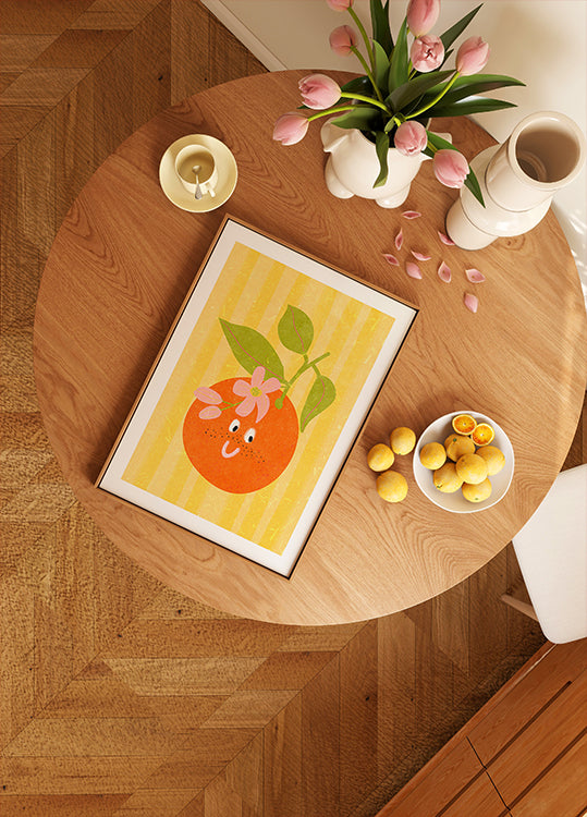 puinen pöytä, jossa on kehystetty appelsiinikuva, kulho sitruunoita, maljakko vaaleanpunaisia ​​tulppaaneja ja kynttilä.